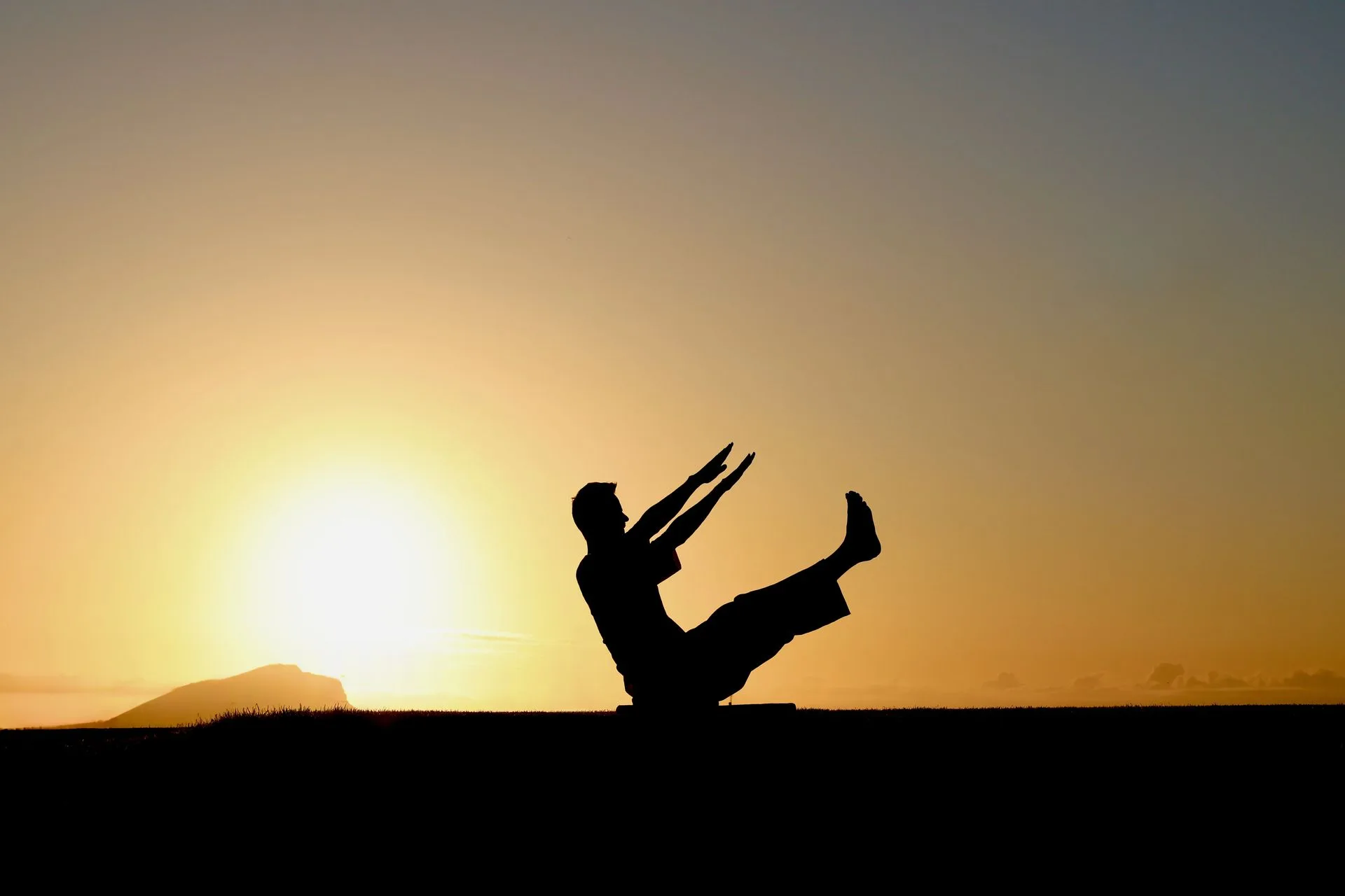 Silhouette in a grounded boat pose at sunset, bare feet against the sky